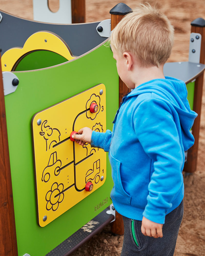 A young boy interacts with a play panel at a playground which is a maze to find animals with a lever.